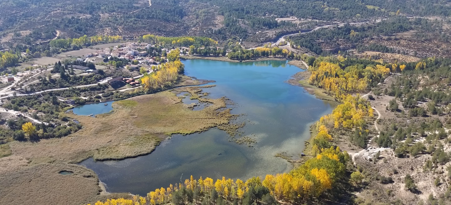 Vista aérea de una laguna rodeada de monte y arbolado de ribera en otoño